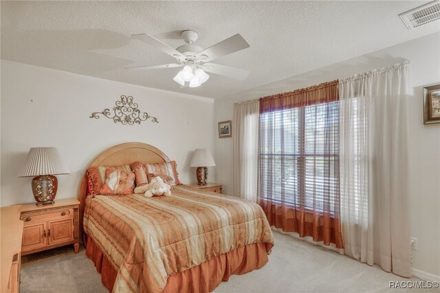 bedroom with a textured ceiling, ceiling fan, visible vents, and light carpet