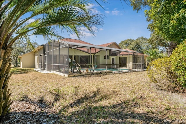 rear view of house with a lanai, a lawn, an outdoor pool, and stucco siding