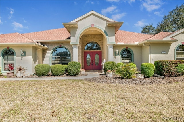 mediterranean / spanish house with brick siding, roof with shingles, and a front yard