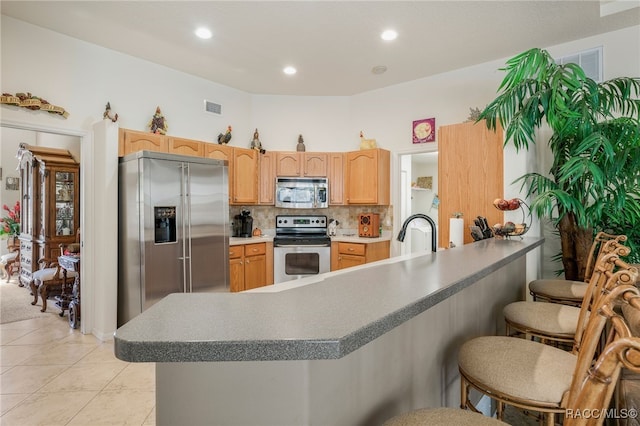 kitchen featuring visible vents, light brown cabinetry, a kitchen breakfast bar, tasteful backsplash, and stainless steel appliances