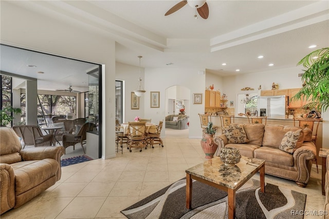 living area with light tile patterned floors, a ceiling fan, recessed lighting, arched walkways, and a raised ceiling