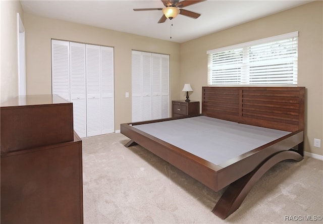 bedroom featuring two closets, light colored carpet, and ceiling fan