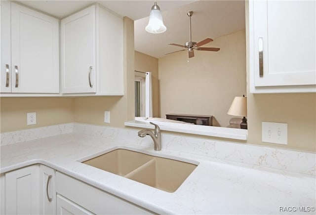 kitchen with sink, white cabinetry, light stone counters, decorative light fixtures, and ceiling fan