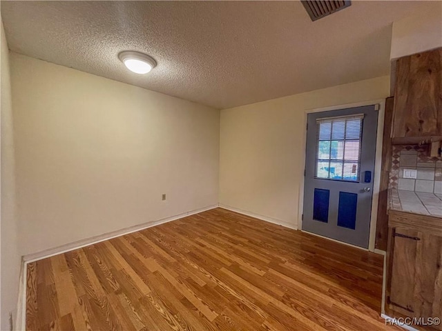 interior space with a textured ceiling, wood finished floors, and visible vents