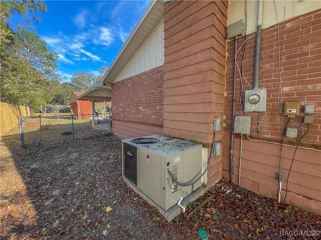 view of property exterior featuring a gate, fence, cooling unit, and brick siding