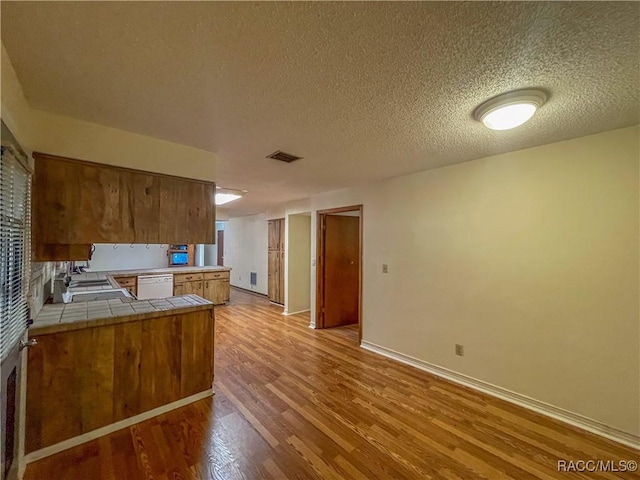 kitchen featuring light wood finished floors, visible vents, brown cabinetry, dishwasher, and tile countertops