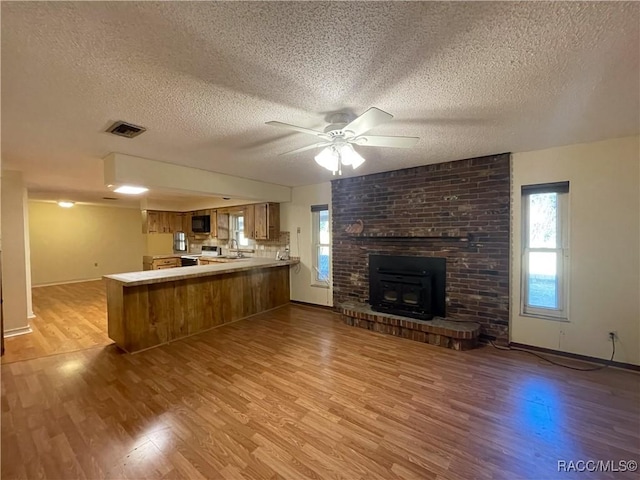 kitchen with visible vents, stainless steel microwave, open floor plan, a peninsula, and light wood-type flooring