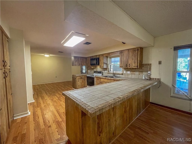 kitchen featuring tile countertops, a peninsula, black microwave, and electric range oven