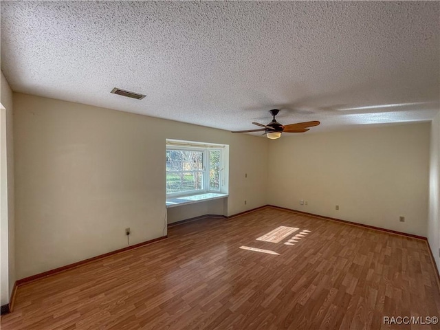 empty room with a textured ceiling, ceiling fan, wood finished floors, visible vents, and baseboards