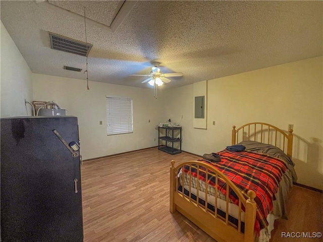 bedroom featuring attic access, electric panel, visible vents, a textured ceiling, and light wood-style floors