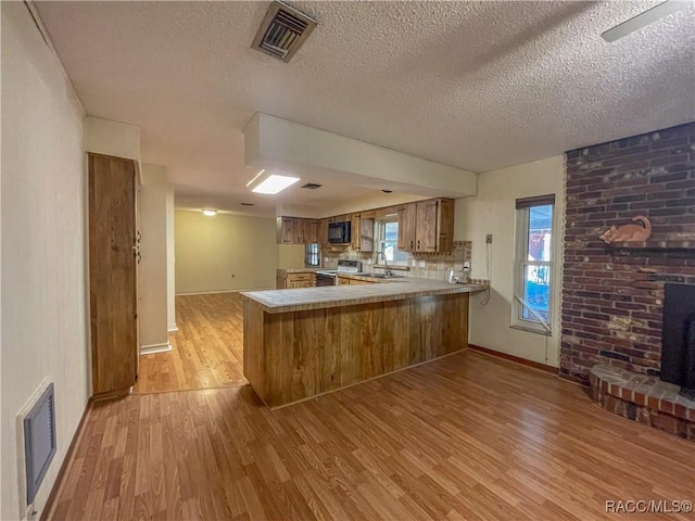 kitchen with a peninsula, a fireplace, visible vents, white range with electric stovetop, and light wood finished floors