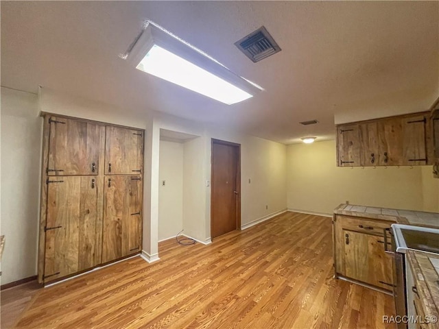 kitchen with visible vents, tile counters, electric range oven, light wood finished floors, and brown cabinetry