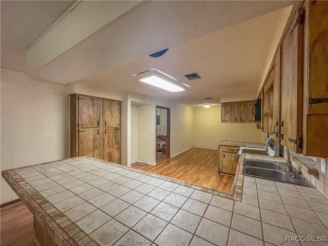 kitchen with brown cabinets, tile countertops, visible vents, a sink, and a textured ceiling