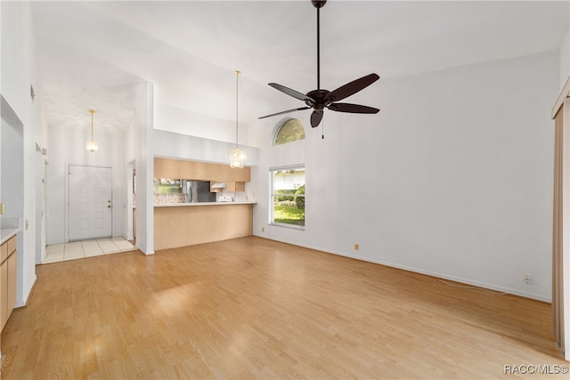 unfurnished living room featuring ceiling fan with notable chandelier, light wood-type flooring, and high vaulted ceiling