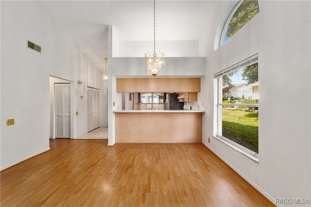 interior space featuring kitchen peninsula, light brown cabinets, an inviting chandelier, light hardwood / wood-style flooring, and a high ceiling