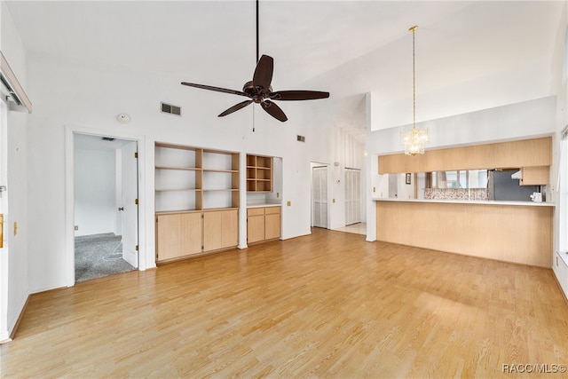 unfurnished living room with ceiling fan with notable chandelier, light wood-type flooring, and high vaulted ceiling