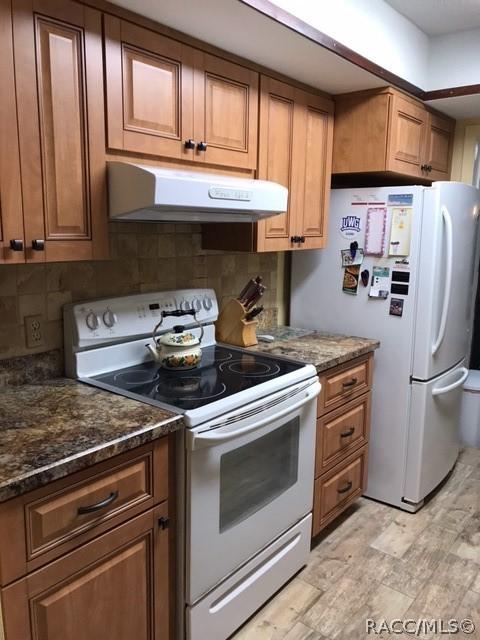 kitchen with decorative backsplash, dark stone counters, and white appliances