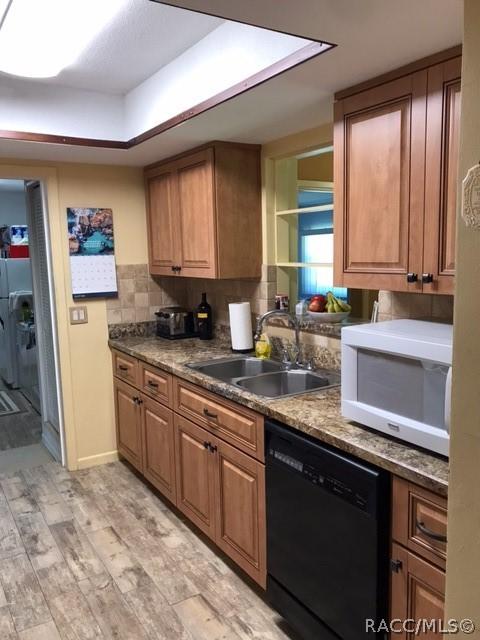 kitchen featuring light wood-type flooring, black dishwasher, decorative backsplash, and sink