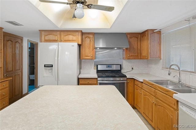 kitchen with white appliances, a raised ceiling, wall chimney range hood, sink, and ceiling fan