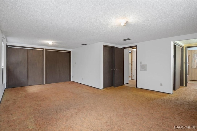 unfurnished bedroom with light carpet, a textured ceiling, and two closets