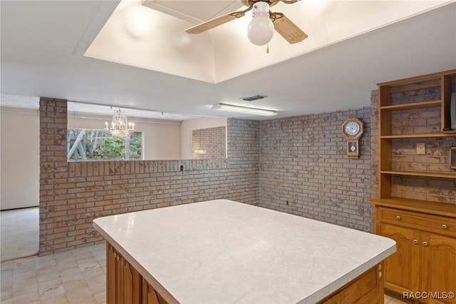 kitchen with ceiling fan with notable chandelier, a kitchen island, hanging light fixtures, and brick wall