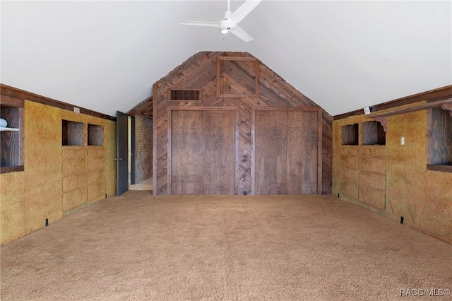 interior space with carpet flooring, ceiling fan, lofted ceiling, and wooden walls