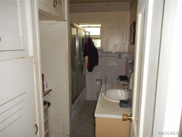 bathroom with vanity, bath / shower combo with glass door, and tile walls