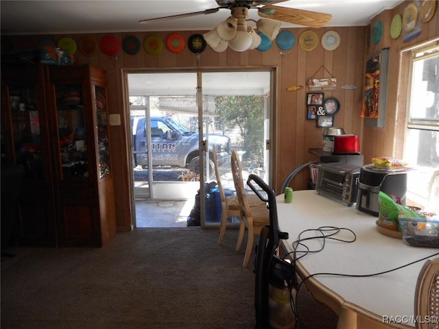 dining area with carpet flooring, a wealth of natural light, ceiling fan, and wood walls