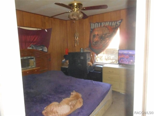 bedroom featuring ceiling fan, a wood stove, a fireplace, and wooden walls