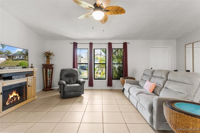 living room with light tile patterned floors, baseboards, a glass covered fireplace, and ceiling fan