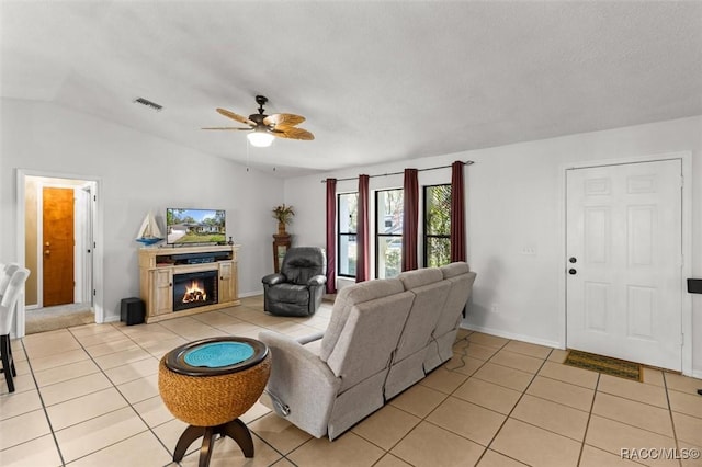 living room with visible vents, ceiling fan, vaulted ceiling, light tile patterned floors, and a warm lit fireplace