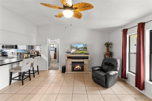 living room with lofted ceiling, a lit fireplace, light tile patterned flooring, baseboards, and ceiling fan