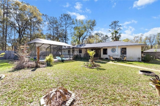 rear view of property featuring glass enclosure, fence, a lawn, and stucco siding