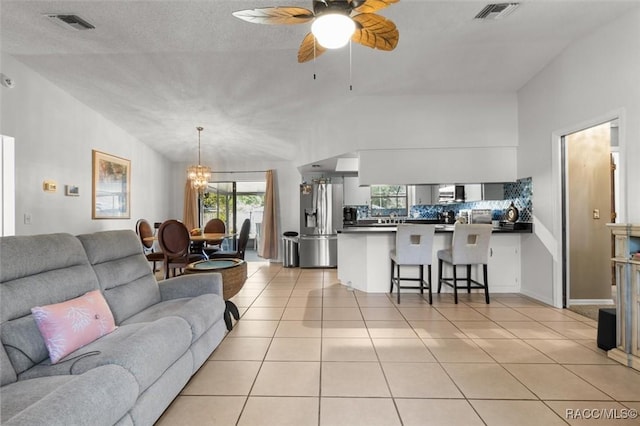 living area with lofted ceiling, light tile patterned floors, ceiling fan with notable chandelier, and visible vents