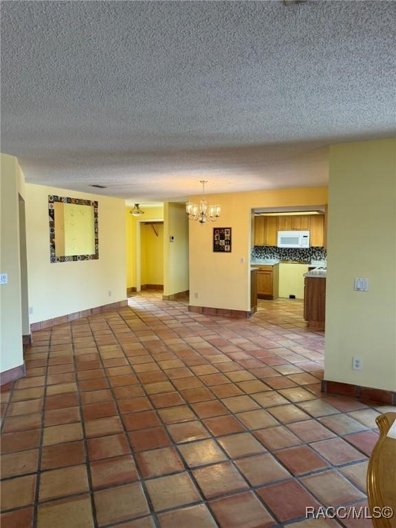 unfurnished living room featuring a textured ceiling, dark tile patterned flooring, and a notable chandelier