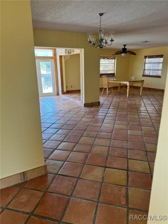 unfurnished room featuring ceiling fan with notable chandelier, a textured ceiling, dark tile patterned flooring, and a healthy amount of sunlight