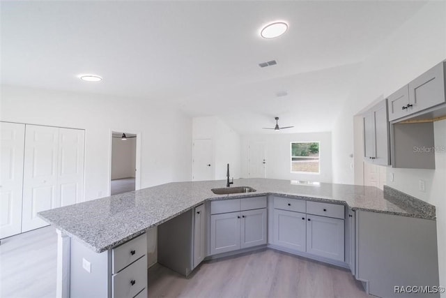 kitchen featuring light stone countertops, gray cabinetry, ceiling fan, a sink, and light wood-style floors
