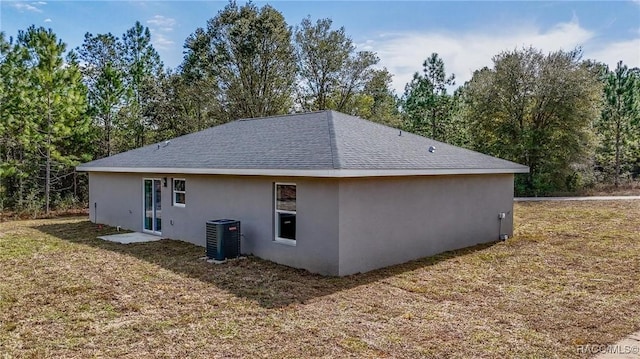 back of property with a yard, a shingled roof, stucco siding, and cooling unit