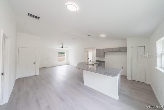 kitchen featuring light wood-style flooring, gray cabinets, visible vents, light stone counters, and lofted ceiling