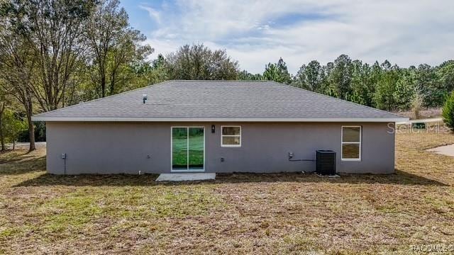 back of property with central air condition unit, stucco siding, and a lawn