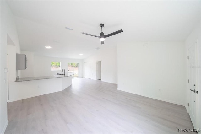 unfurnished living room with a sink, lofted ceiling, wood finished floors, a ceiling fan, and baseboards