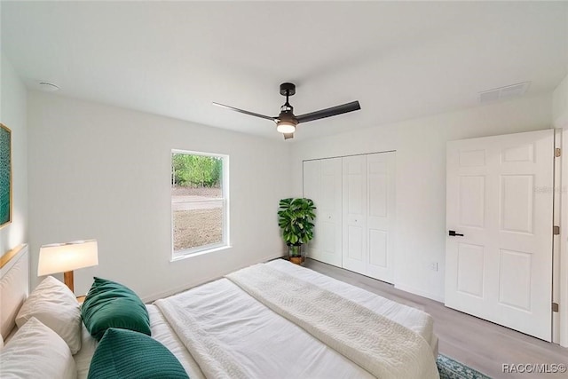 bedroom with a closet, wood finished floors, visible vents, a ceiling fan, and baseboards