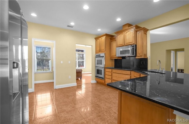 kitchen featuring sink, tasteful backsplash, appliances with stainless steel finishes, kitchen peninsula, and dark stone counters