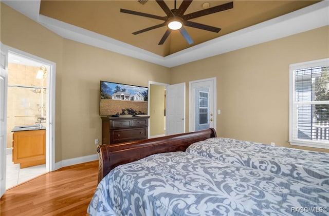 bedroom with ceiling fan, ensuite bathroom, light wood-type flooring, and a tray ceiling