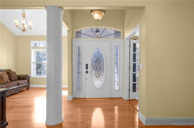 foyer entrance with decorative columns, lofted ceiling, a chandelier, and light hardwood / wood-style flooring