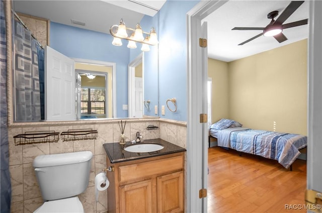 bathroom with hardwood / wood-style floors, tile walls, vanity, ceiling fan, and toilet