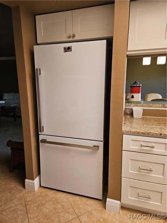 kitchen with light tile patterned flooring, white cabinetry, and freestanding refrigerator