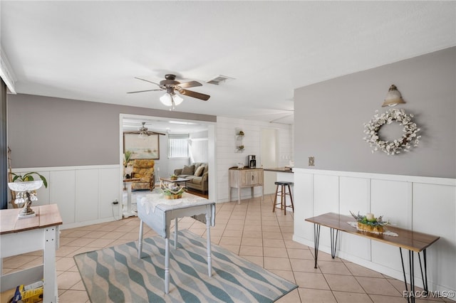 interior space with light tile patterned floors, a ceiling fan, visible vents, and wainscoting