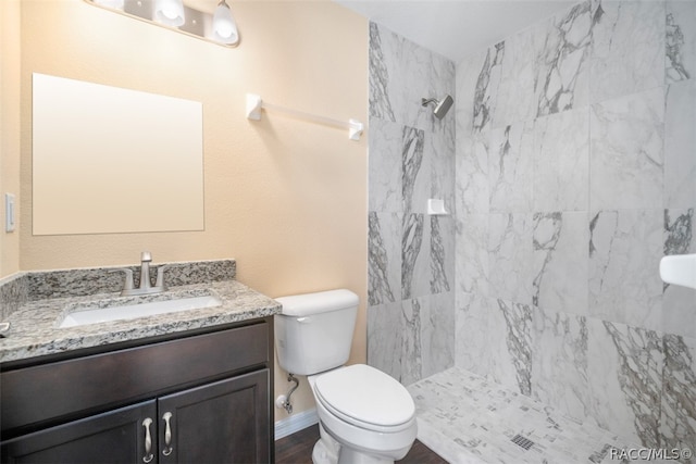 bathroom with a tile shower, vanity, and toilet