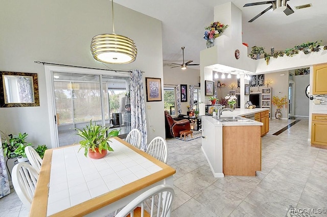 kitchen featuring a center island with sink, ceiling fan, light brown cabinetry, high vaulted ceiling, and decorative light fixtures